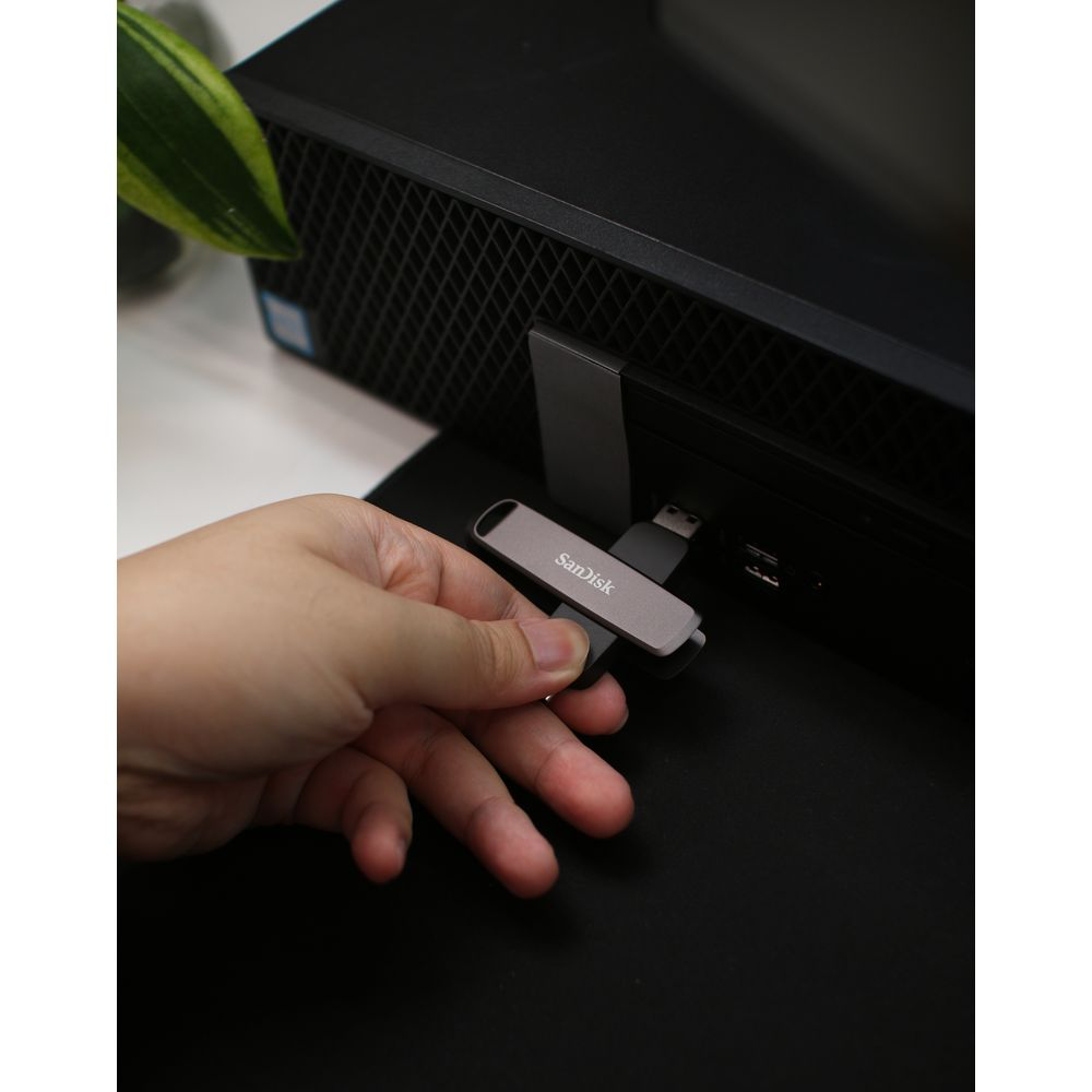 Una mano tiene un'unità USB SanDisk grigia accanto a una torre del computer.
