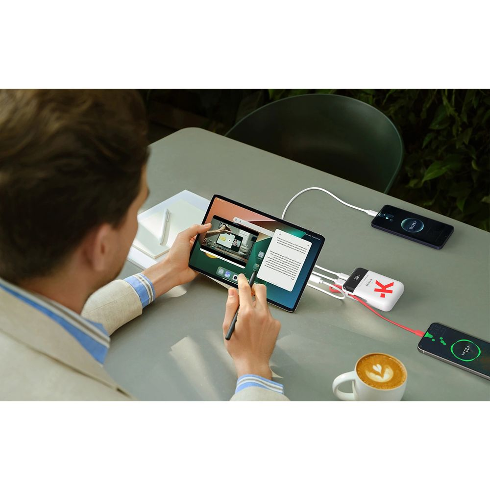 Homme utilise tablette, chargeur et deux téléphones sur table avec café.