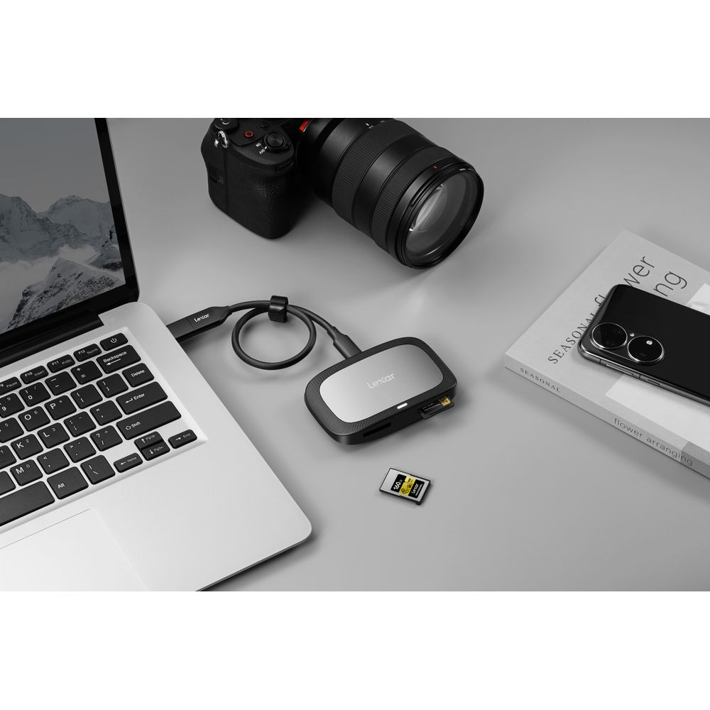 Laptop, lettore di schede, fotocamera, scheda SD e libri su superficie grigia.