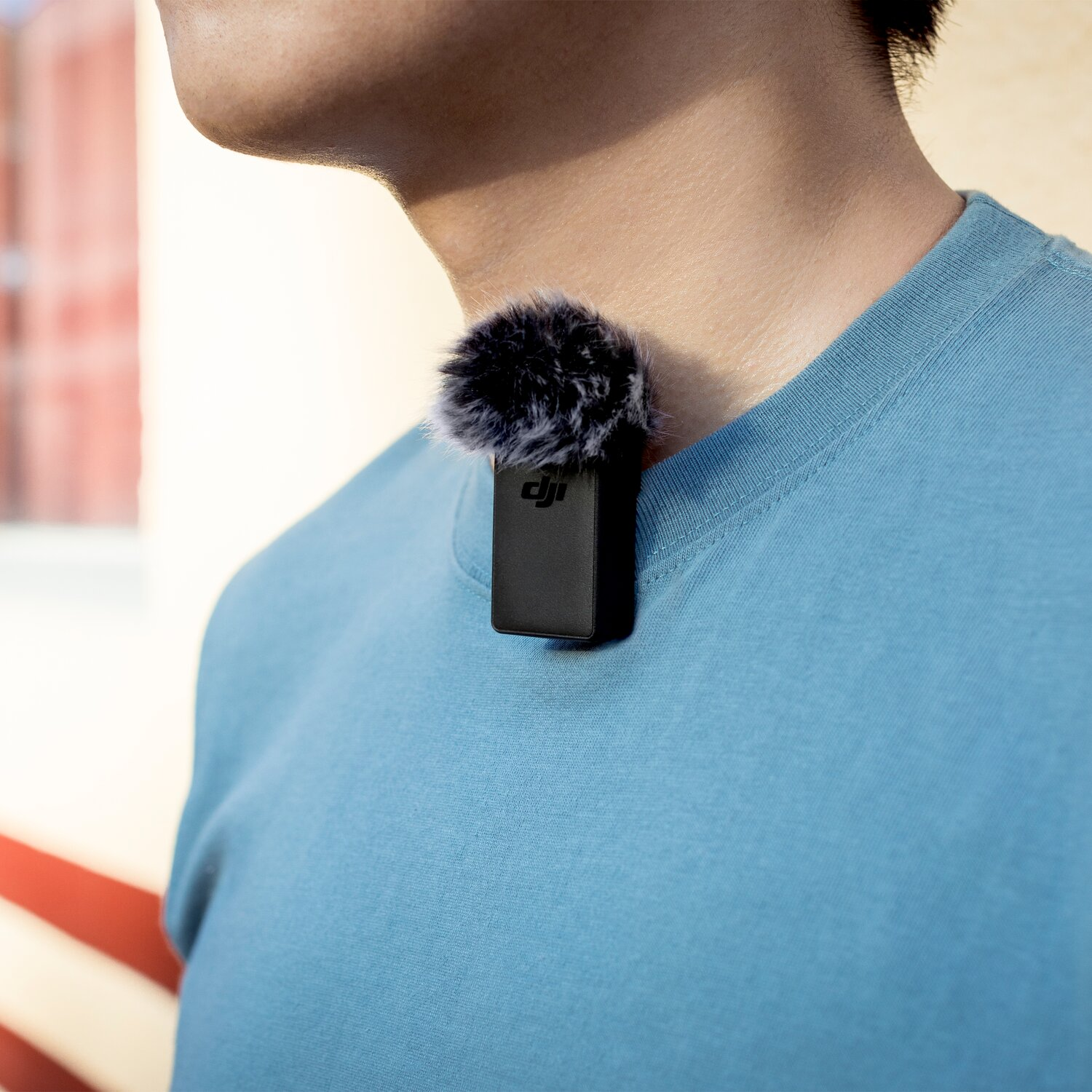 Ein DJI-Mikrofon mit pelzigem Windschutz ist am Kragen eines blauen T-Shirts befestigt.