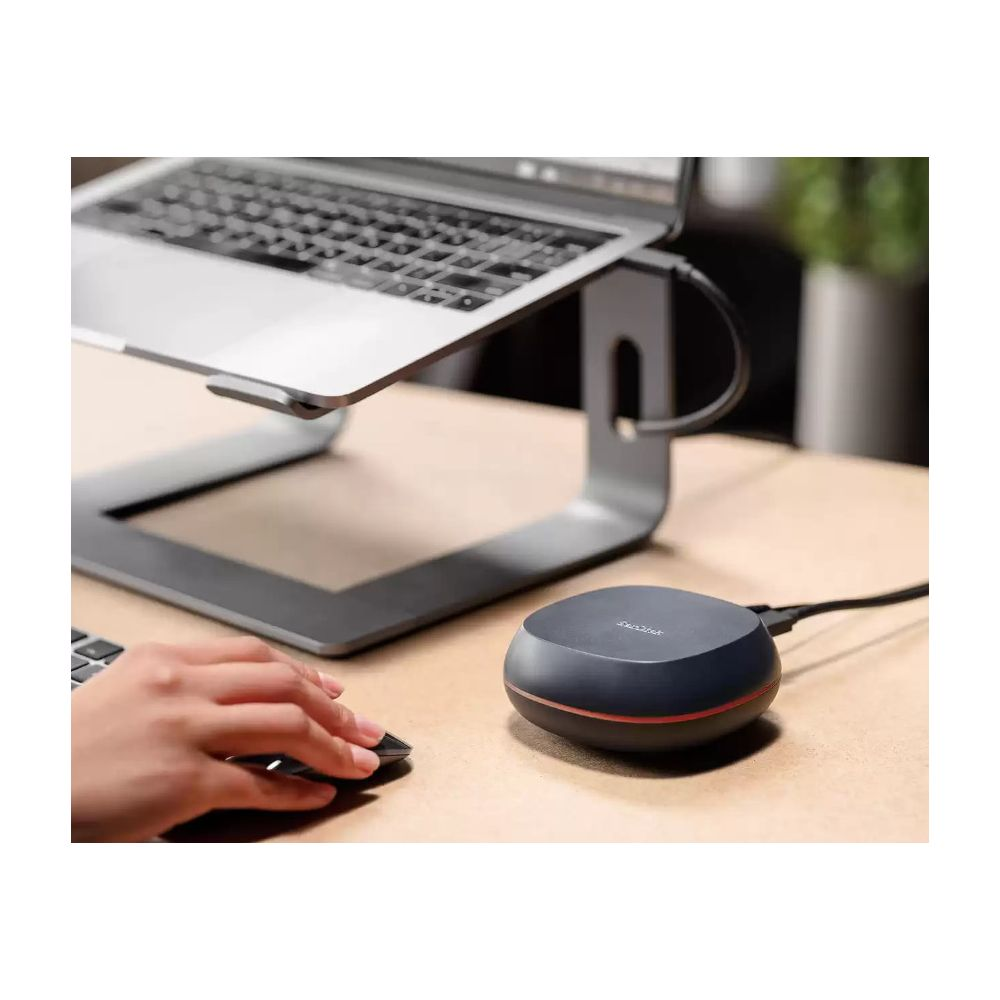 A laptop sits on a stand. A hand uses a mouse. A black round object is nearby.