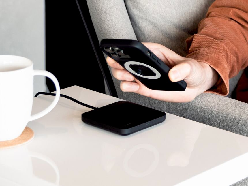 Una persona tiene uno smartphone nero sopra un caricabatterie wireless nero.