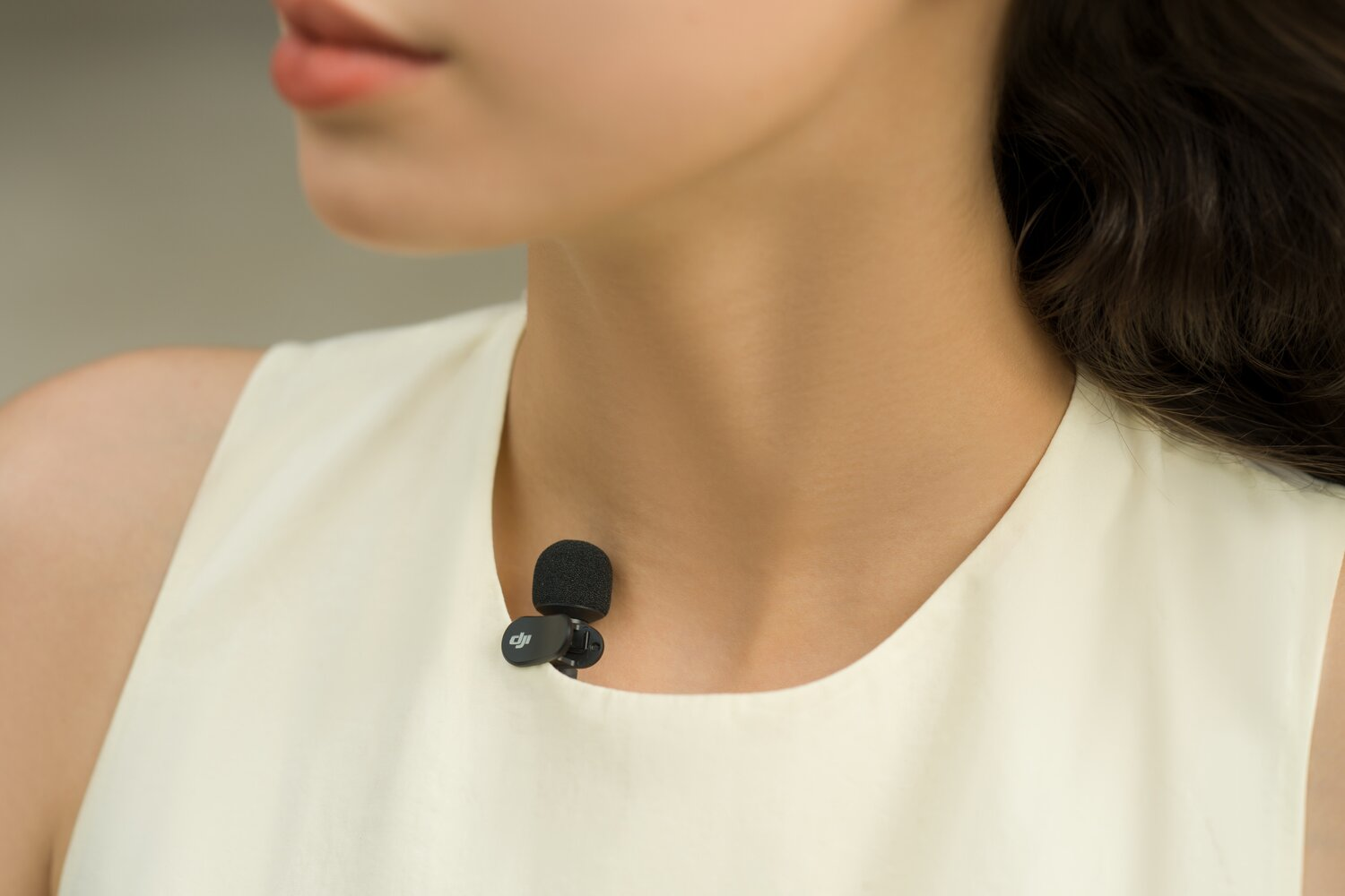 Ein schwarzes Ansteckmikrofon mit DJI-Logo ist an einem cremefarbenen Kleid befestigt.