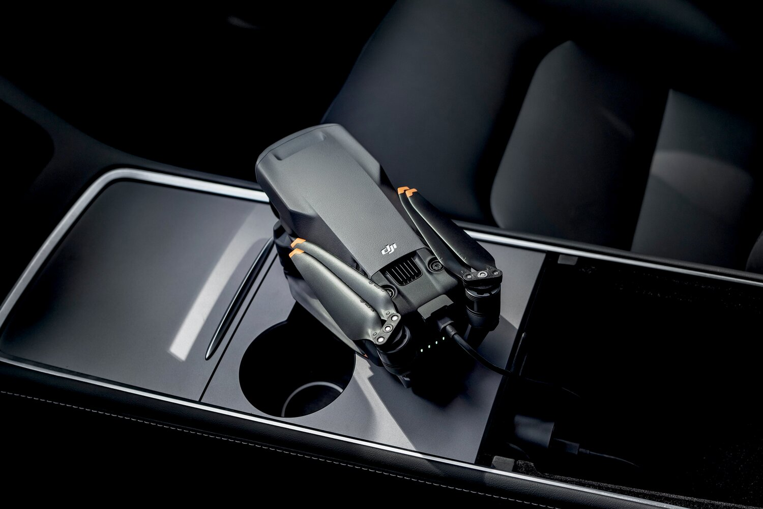 Ein graues DJI-Drohnenmodell liegt auf einem schwarzen Autoinnenraum-Konsolenbereich.