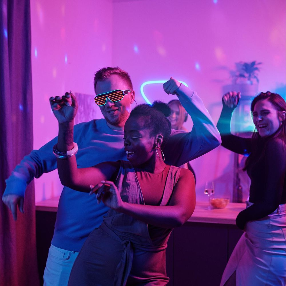 Leute tanzen auf einer Party mit Neonlichtern und bunter Beleuchtung.