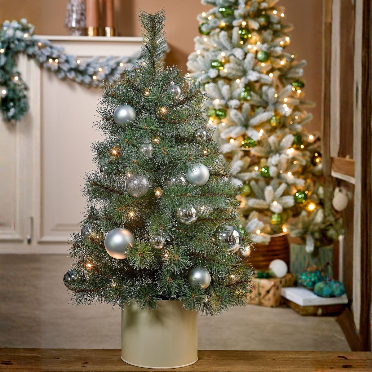 A small Christmas tree with silver ornaments and lights stands in the foreground.
