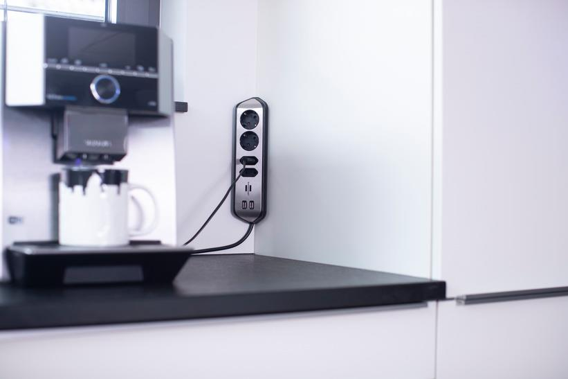 Kaffeemaschine brüht in eine Tasse, Steckdosenleiste an der Wand.