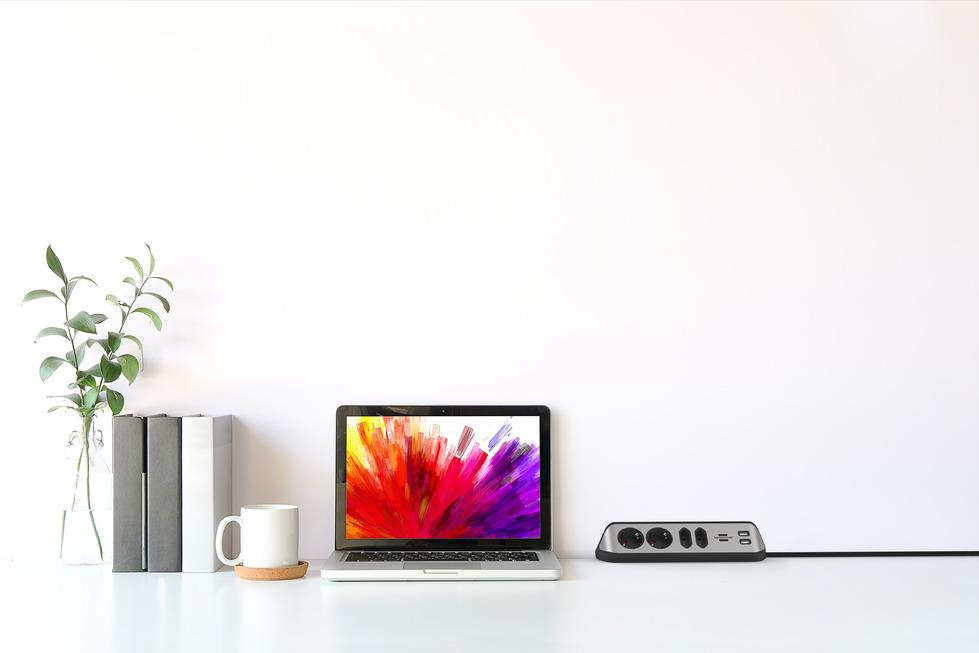 Ein Laptop mit buntem Bildschirm steht neben einer Tasse und Büchern auf einem Schreibtisch.