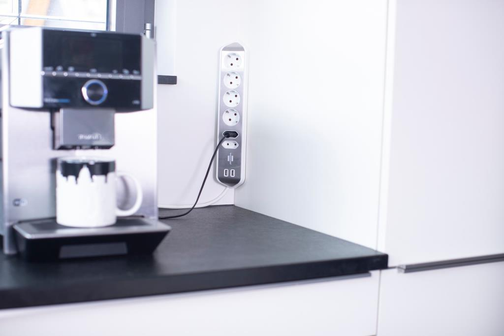Kaffeemaschine mit Tasse und Steckdosenleiste an der Wand.