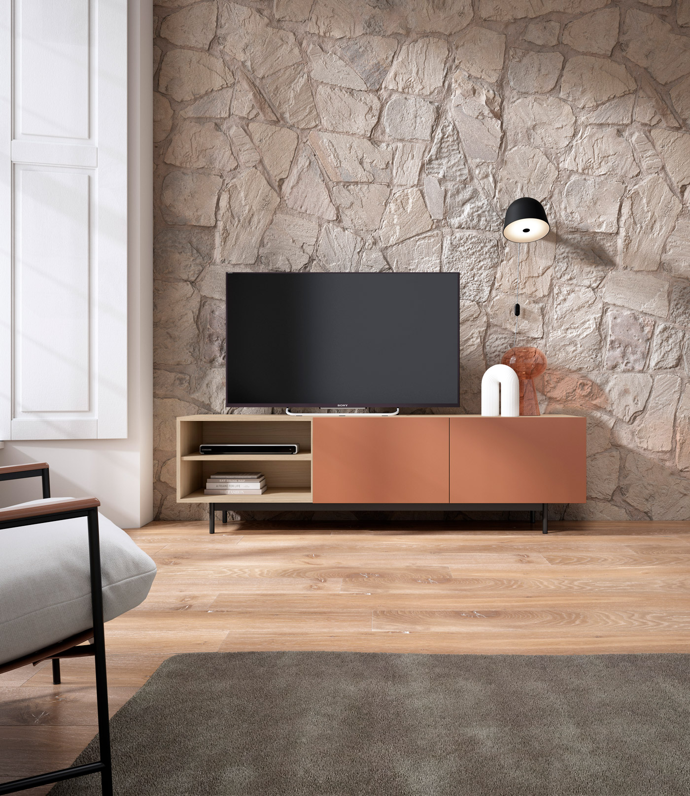 Mueble de TV con televisor frente a pared de piedra. Sillón y alfombra.