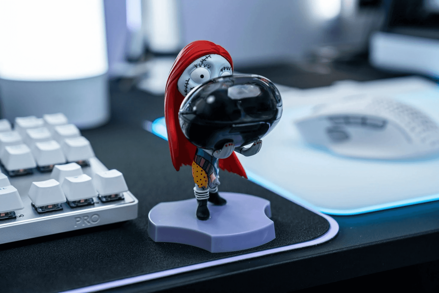 Figura de Sally con pelo rojo y vestido patchwork sostiene esfera negra en escritorio.