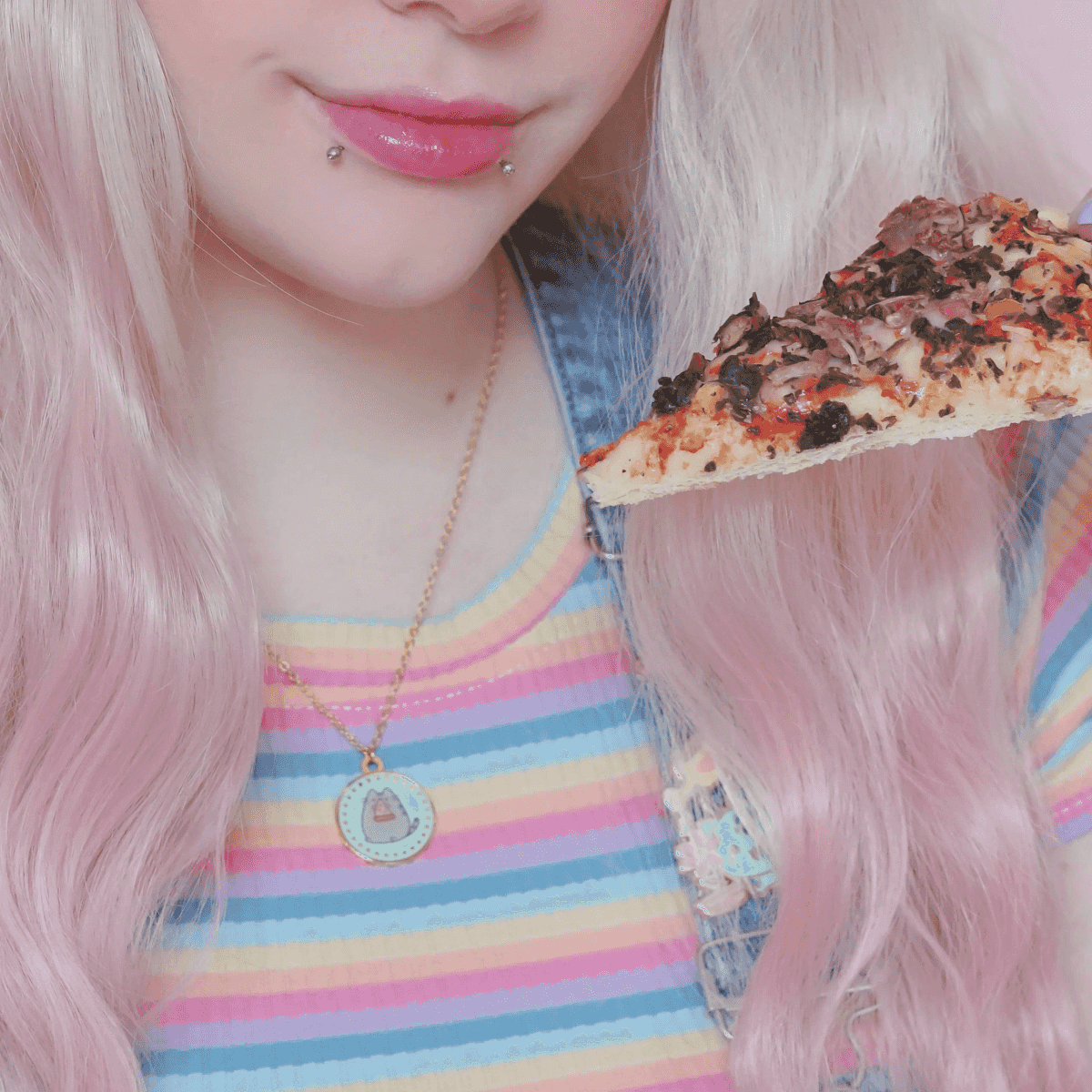 Persona con pelo rosa sostiene una rebanada de pizza con ingredientes.