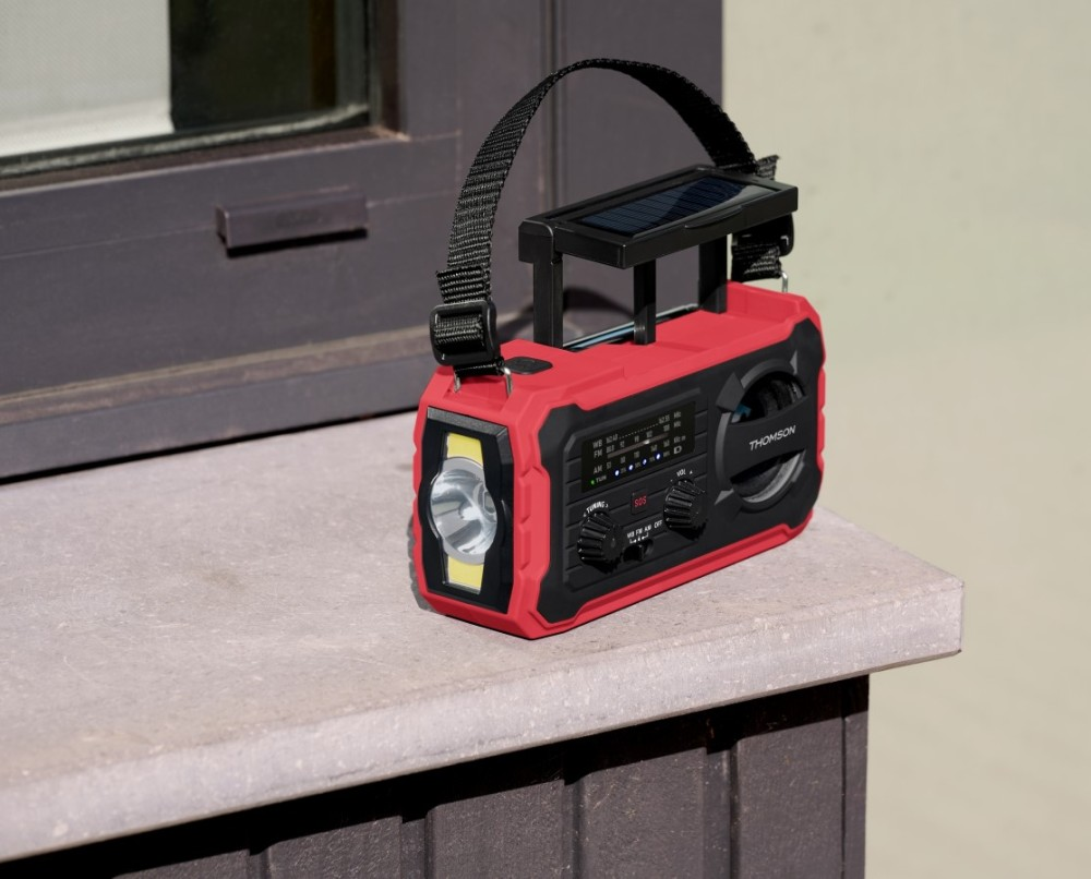 Una radio di emergenza Thomson rossa con pannello solare e torcia si trova su una superficie di pietra.