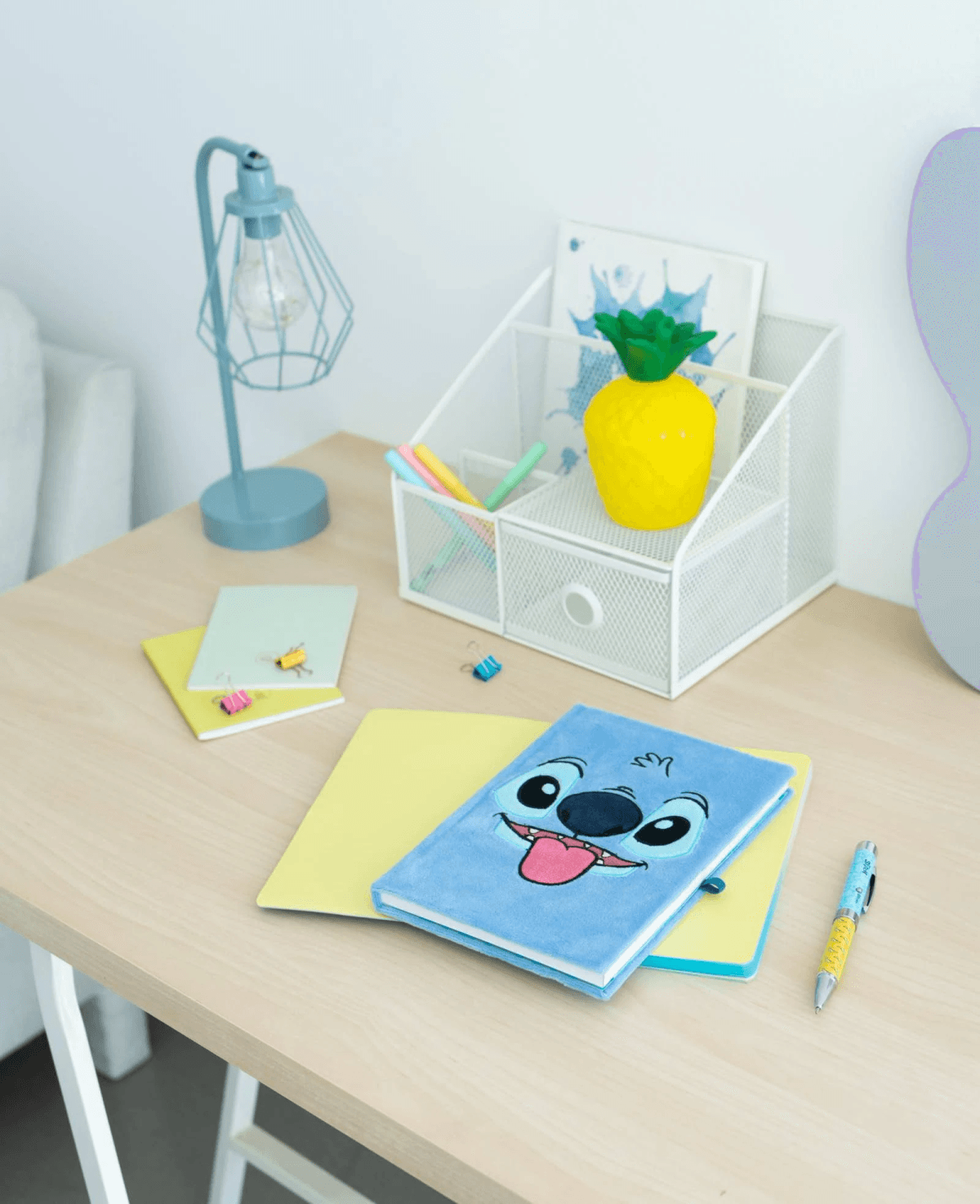 Un cuaderno azul de Stitch está sobre un cuaderno amarillo en un escritorio de madera.
