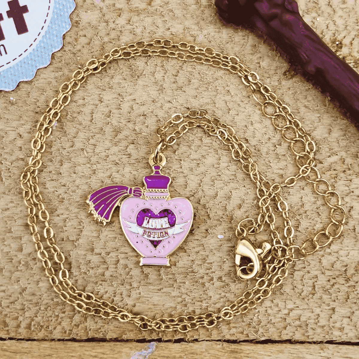 Collar de oro con colgante de botella de poción de amor rosa sobre fondo de madera.