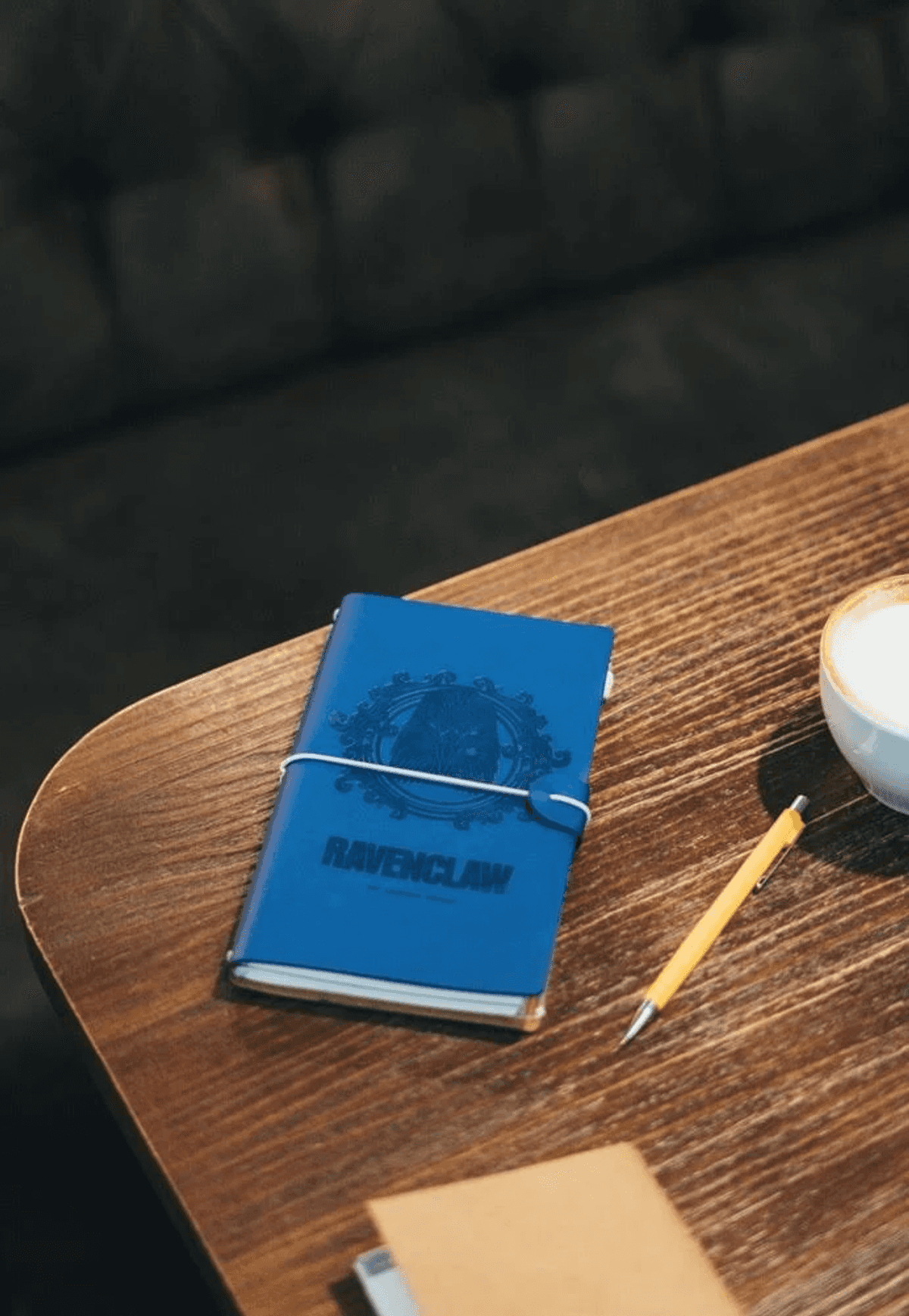 Blauer Ravenclaw-Notizblock mit Stift und Kaffee auf Holztisch.