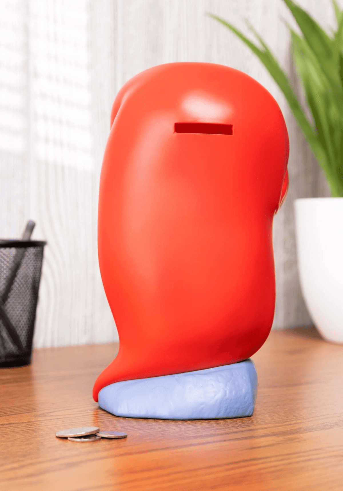 Una hucha roja con forma de cabeza se sienta sobre una base azul con monedas.
