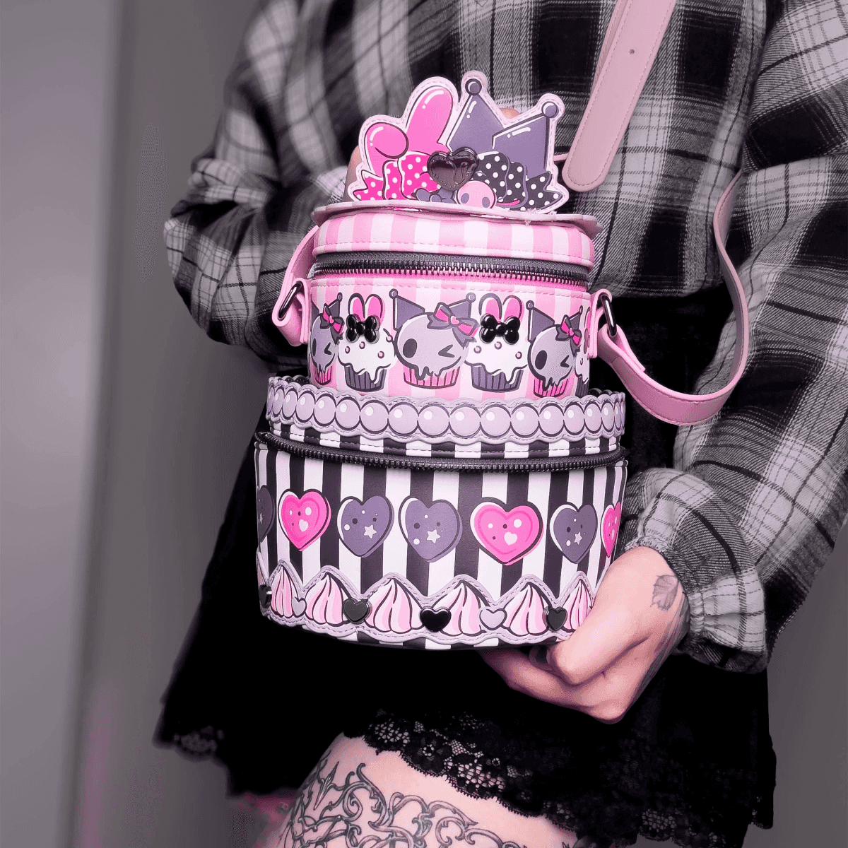 Persona sosteniendo un bolso apilado rosa y negro con cupcakes, coronas y corazones.