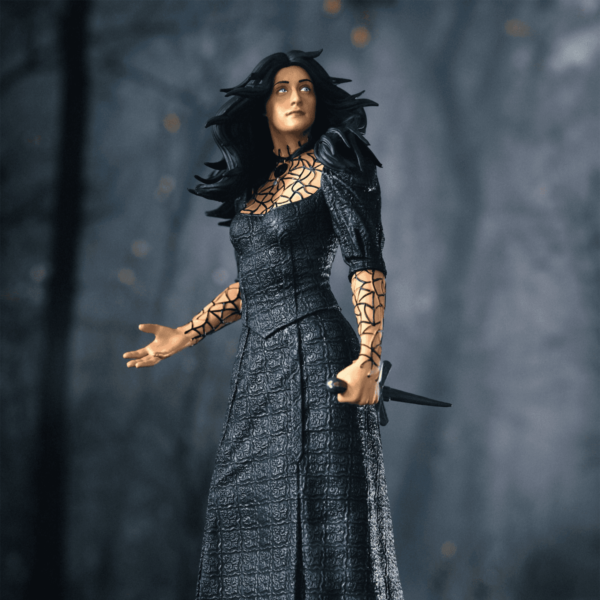 Una mujer con un vestido negro de intrincados patrones y una daga.