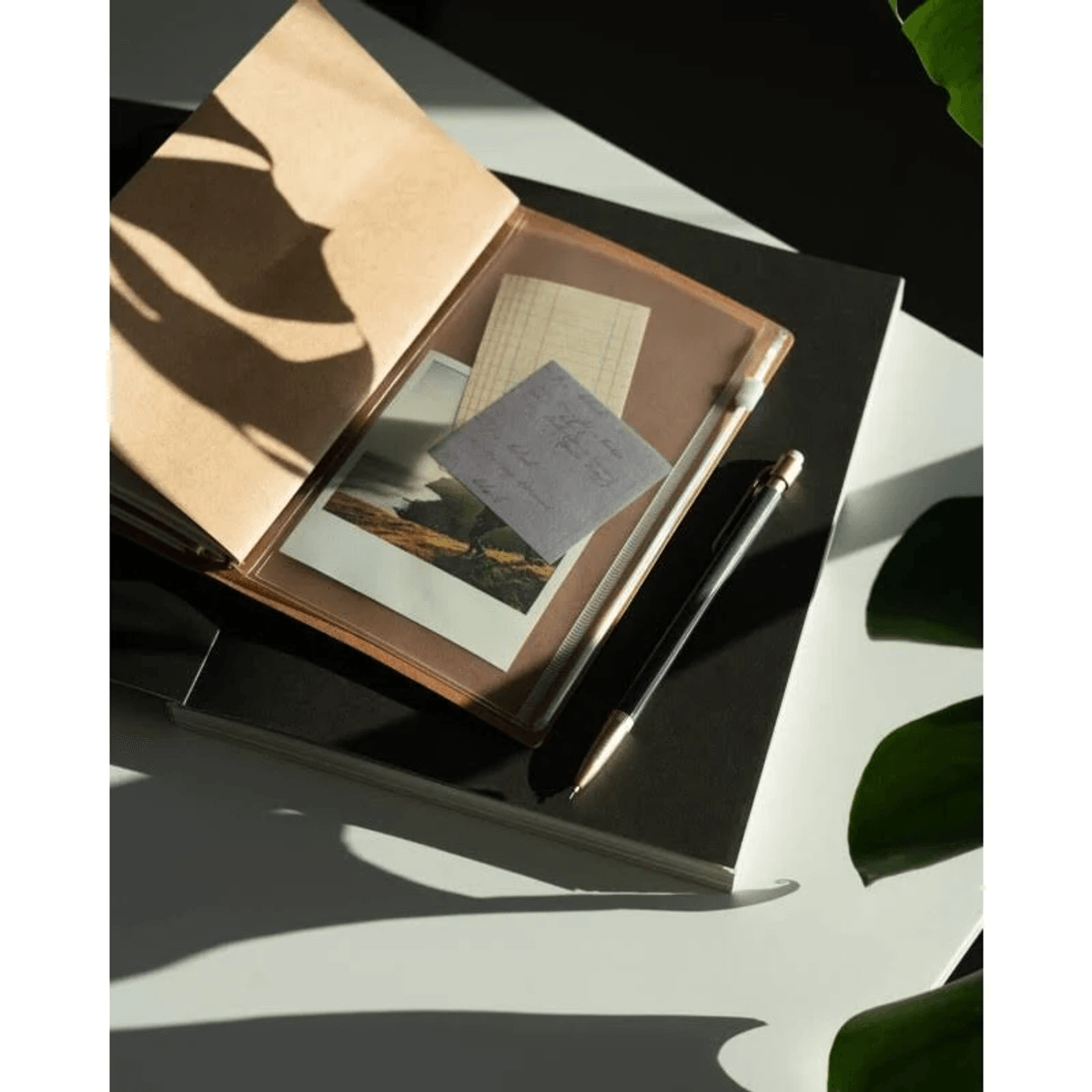 Notizbuch mit Fotos, Notizen und Stift auf Schreibtisch mit Schatten.