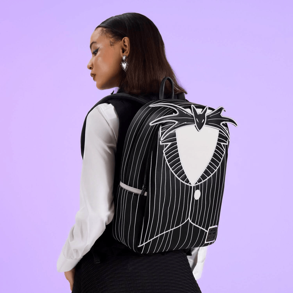Una mujer con una mochila temática de Jack Skellington sobre fondo morado.