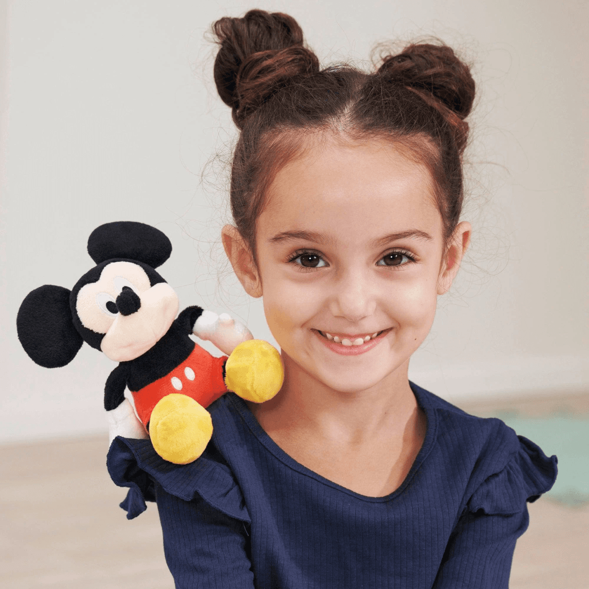 Una niña con moños de' espacio sostiene un peluche de Mickey Mouse en su hombro.