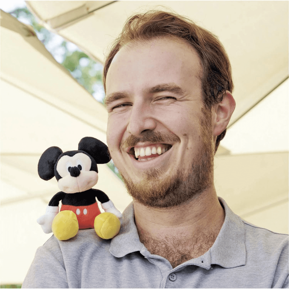 Un hombre sonriente con un peluche de Mickey Mouse en el hombro.