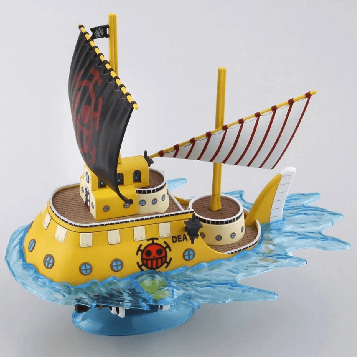 Gelbes Modellschiff mit schwarzen und rot-weißen Segeln auf blauem Wasser.