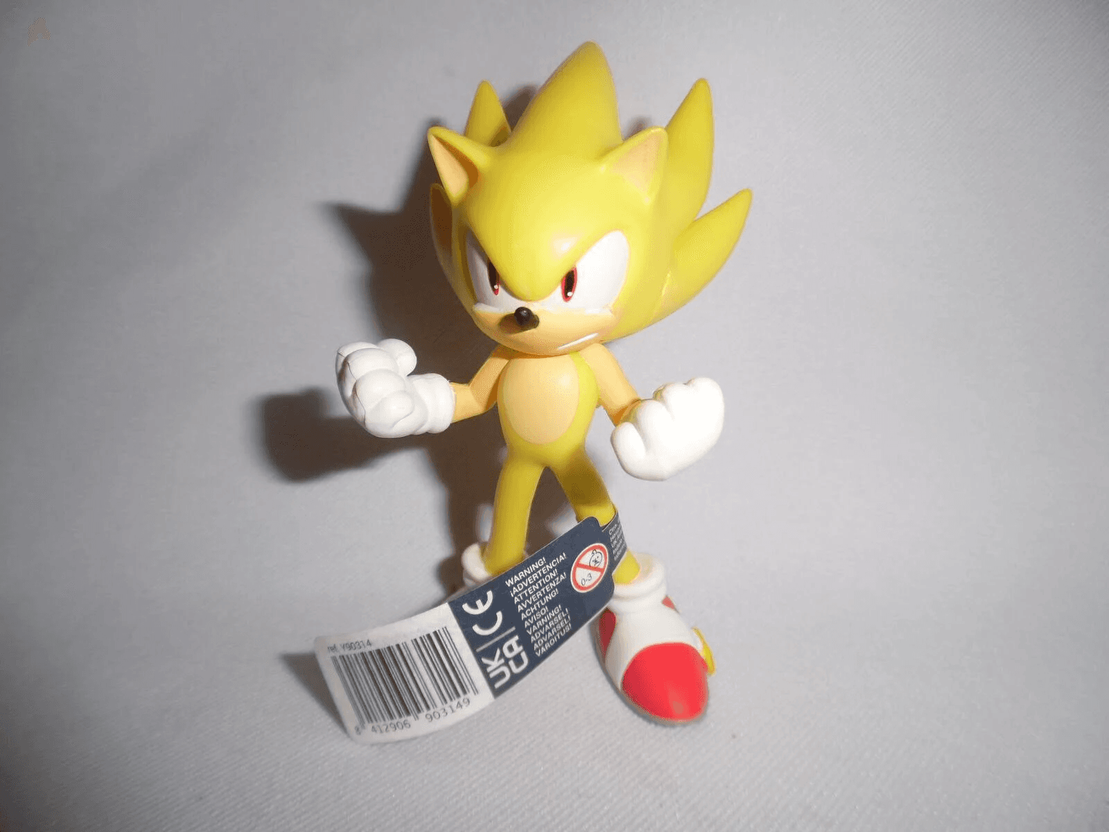 Super Sonic Actionfigur in Gelb mit roten Schuhen und Warnetikett am Fuß.