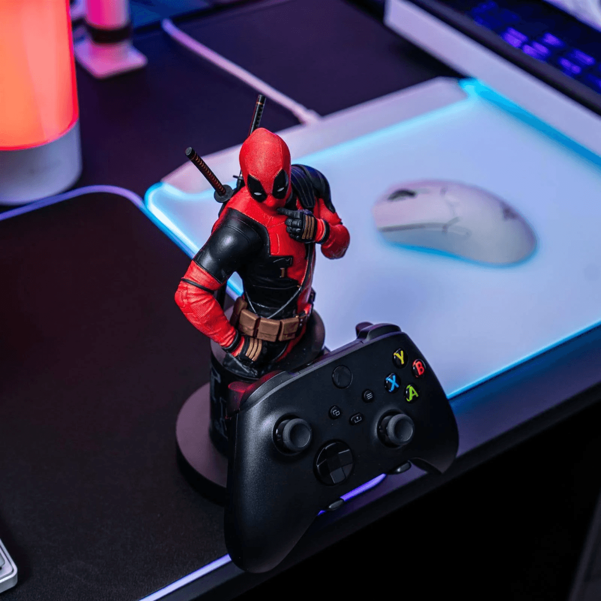 Figura de Deadpool con mando y ratón en un escritorio, iluminado.