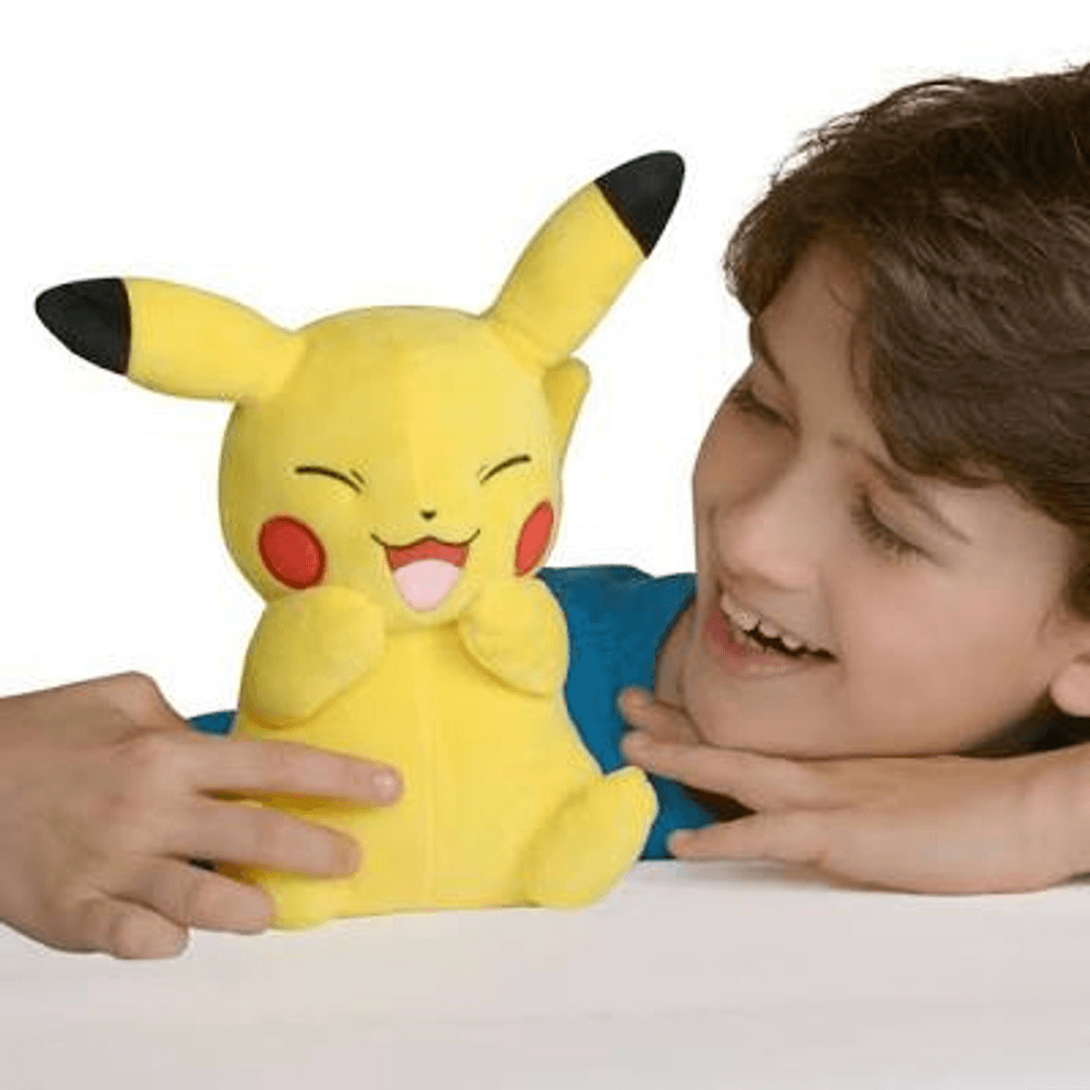 Un niño sonríe junto a un juguete de peluche Pikachu amarillo sentado en una mesa.