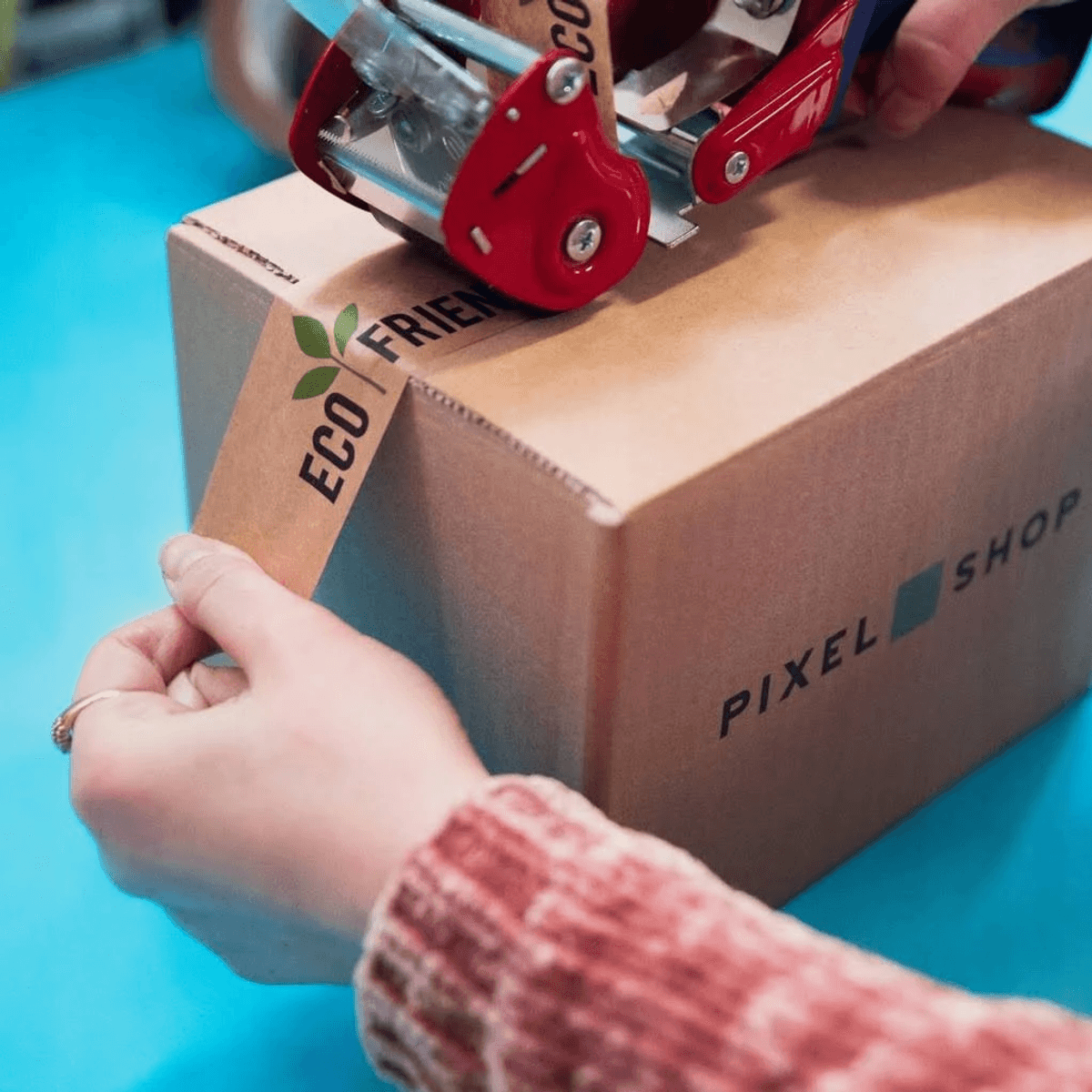 Hände kleben eine umweltfreundliche Box mit Klebeband, 'Pixel Shop'-Logo.