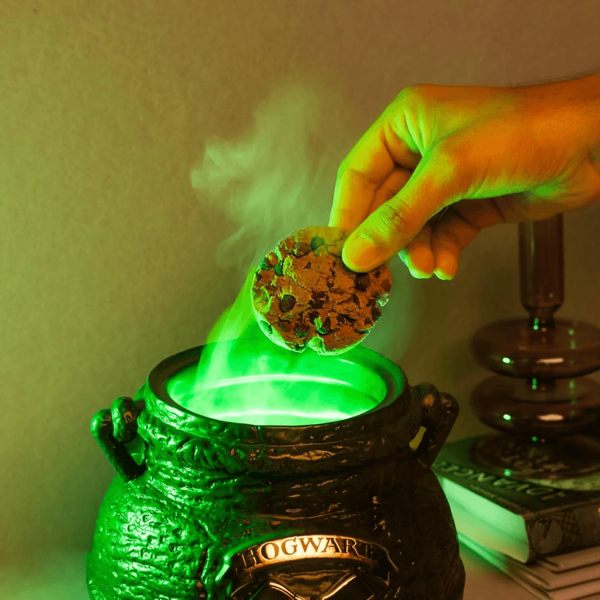 Una mano sostiene una galleta sobre un caldero verde brillante que emite humo.