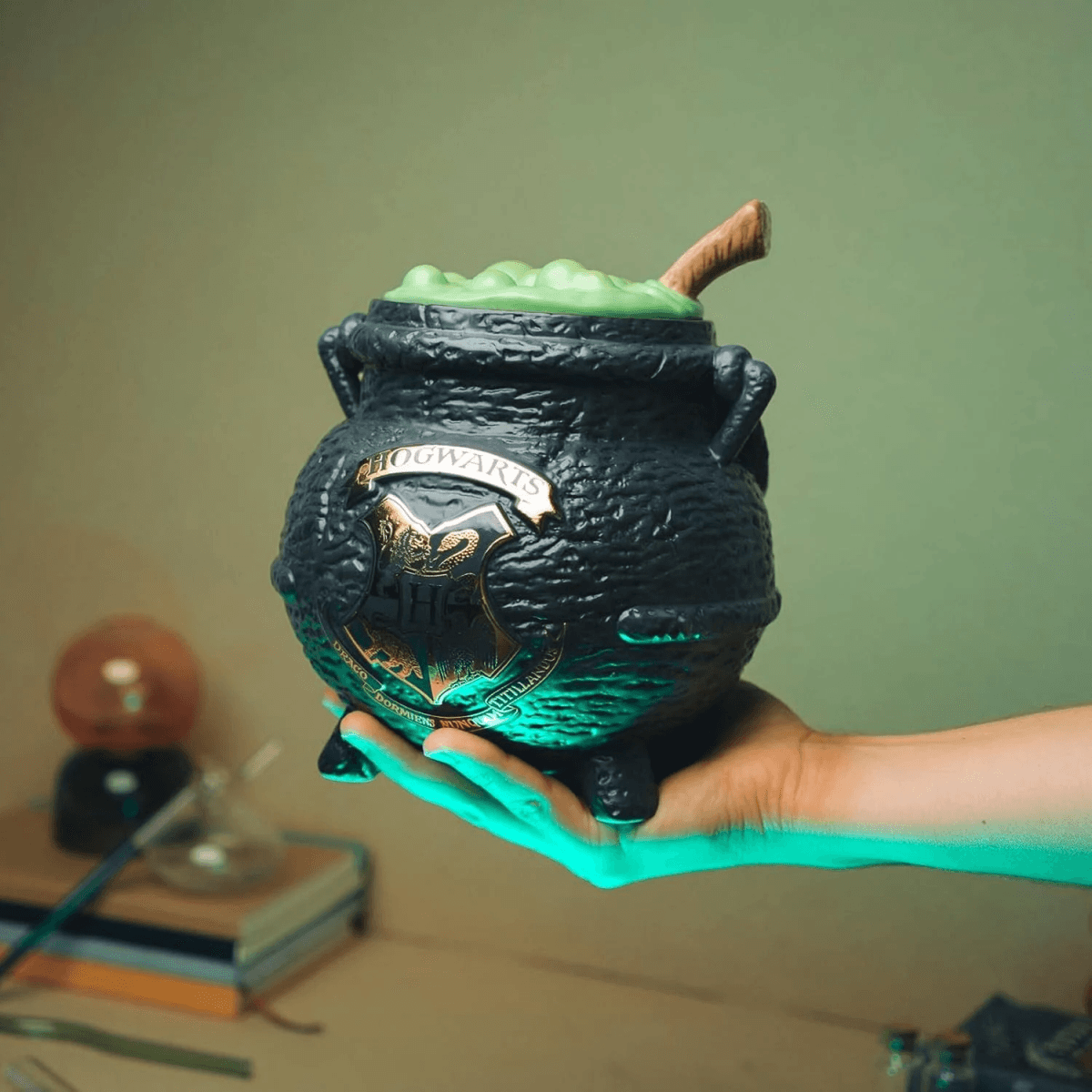 Un caldero negro de Hogwarts con líquido verde y una cuchara de madera sostenido por una mano.