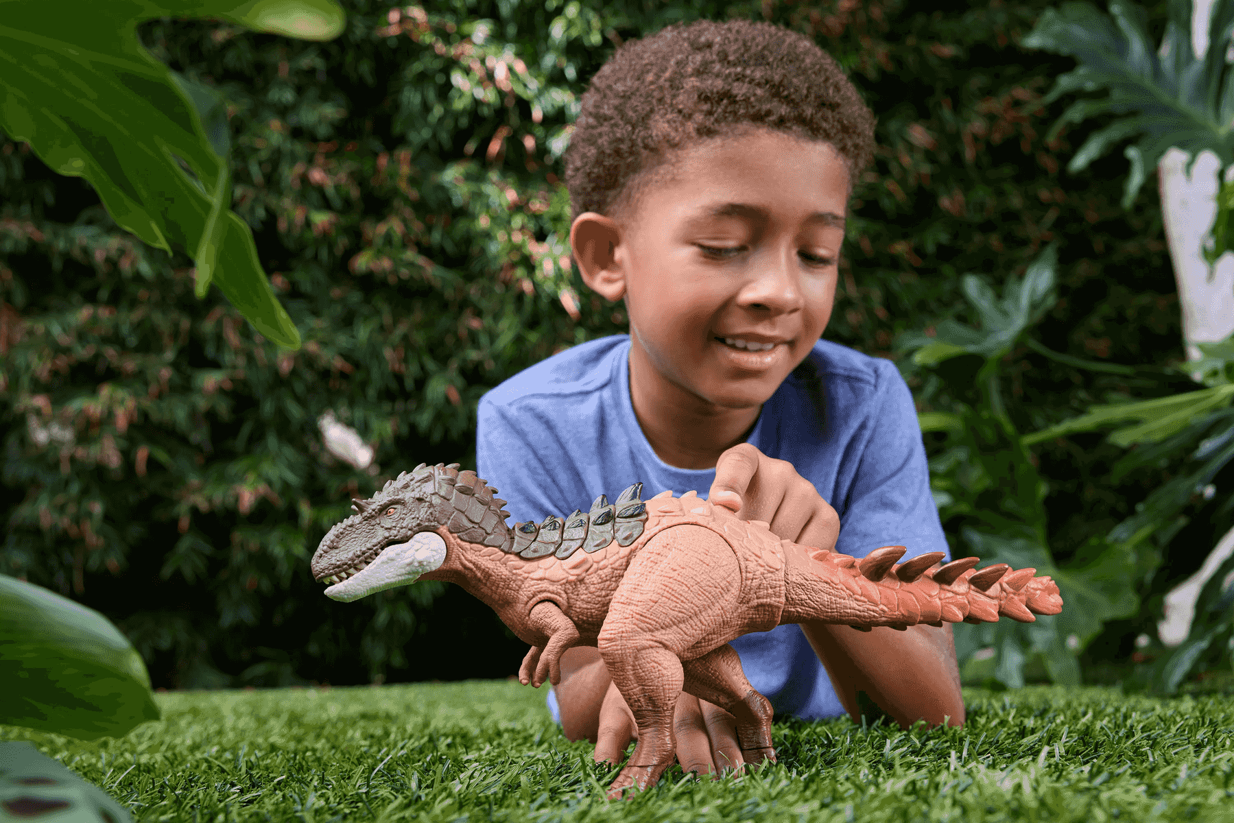 Ein Junge spielt mit einer Dino-Figur im Garten auf dem Gras.