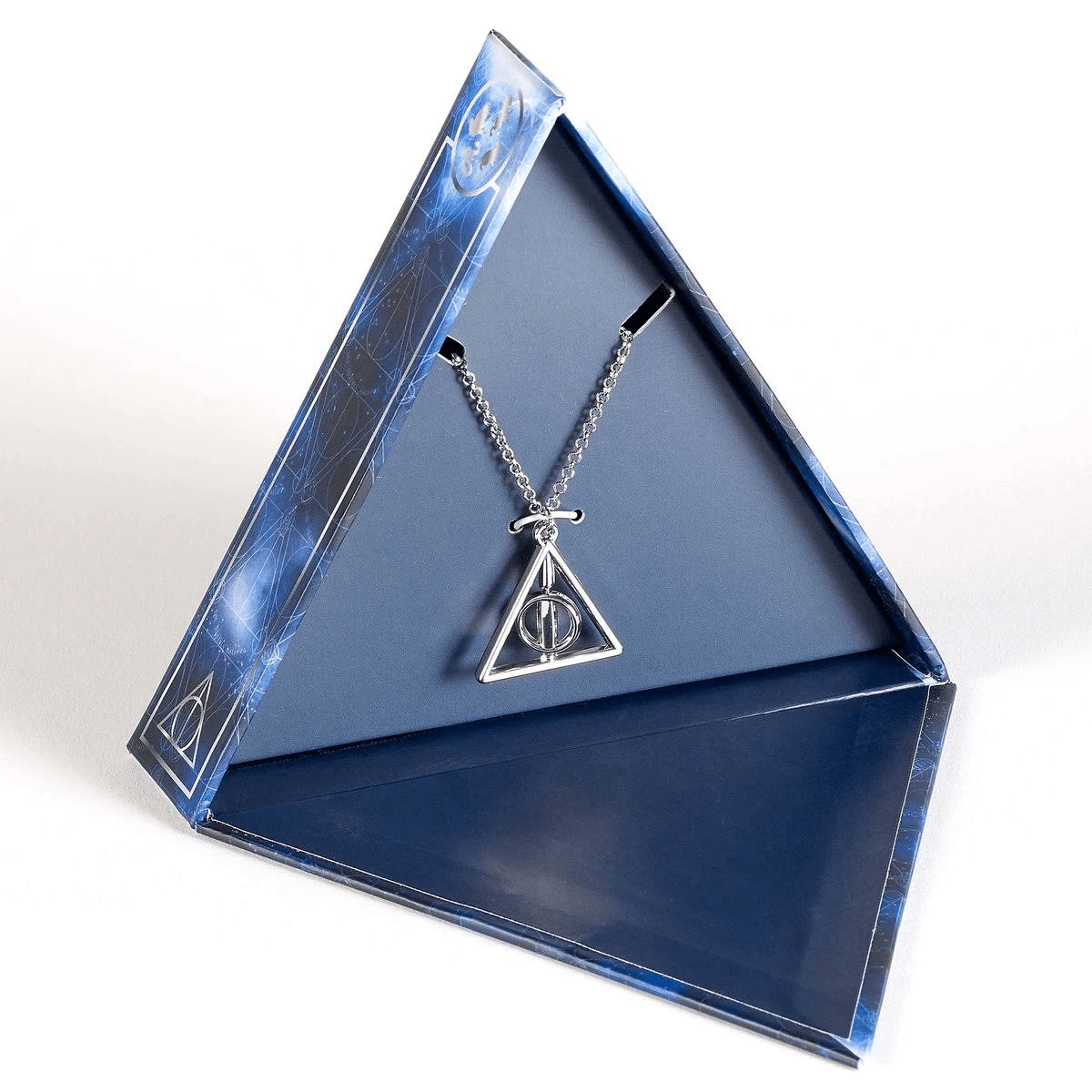 Collar plateado de las Reliquias de la Muerte en una caja triangular azul oscuro abierta con patrones celestes.