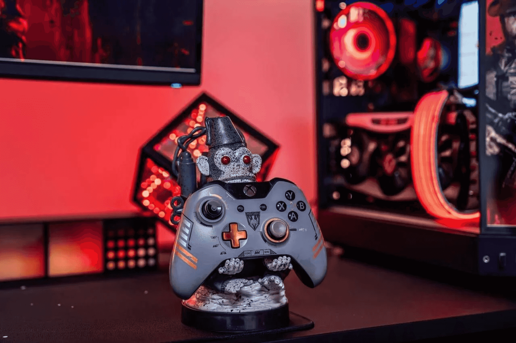 Un soporte de mando de mono con ojos rojos está frente a una PC gamer con ventiladores rojos.