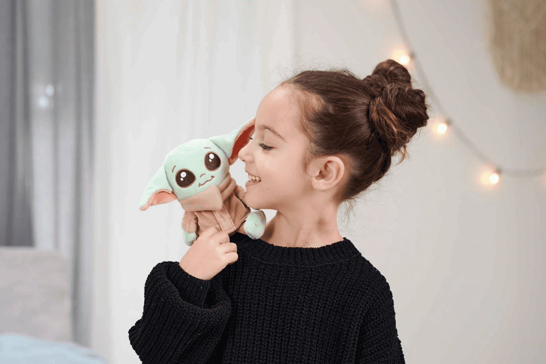 Una niña con un suéter negro sostiene un peluche verde en su hombro.
