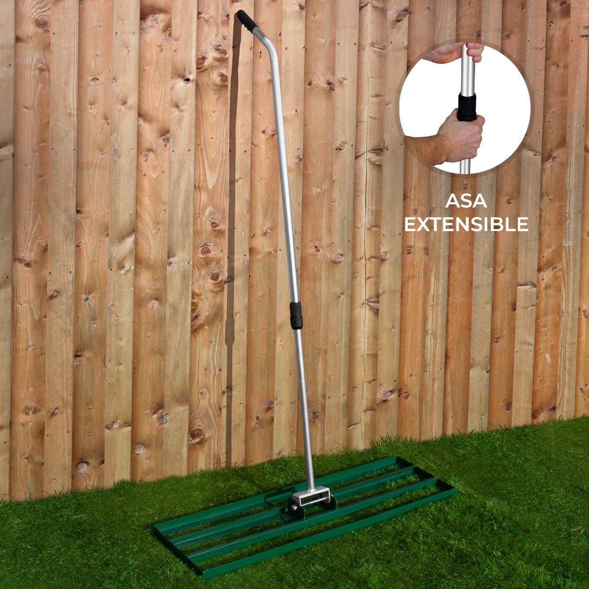 Un rastrillo extensible con cabeza verde frente a una valla de madera.