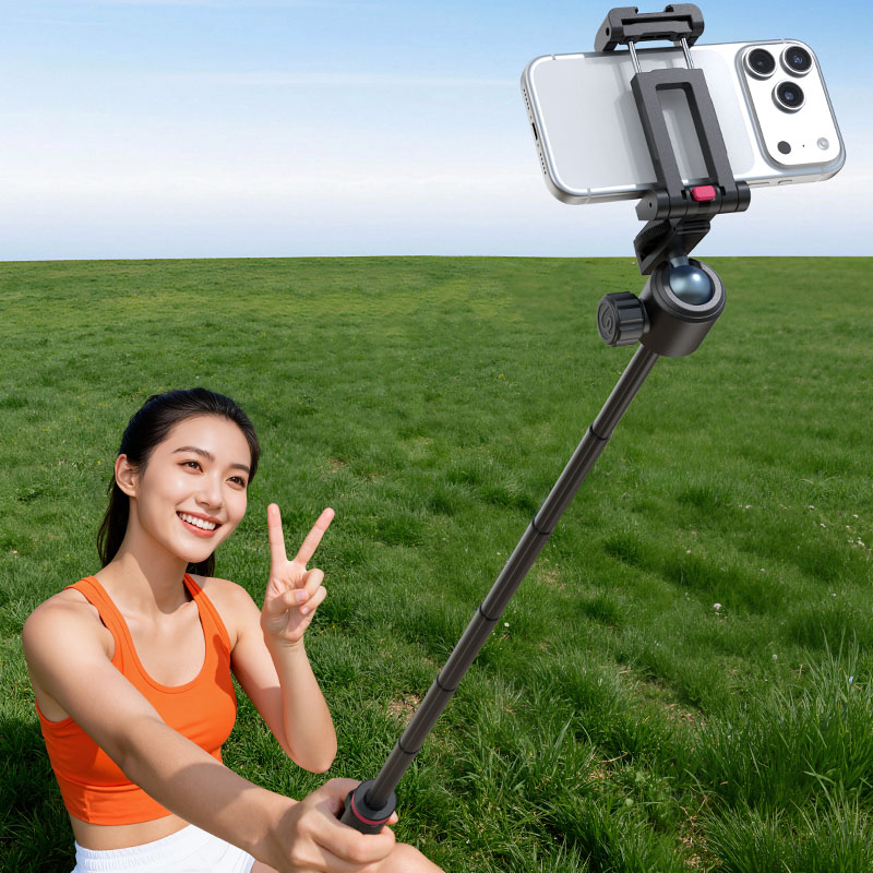 Una mujer se toma una selfie con un palo selfie en un campo verde bajo un cielo azul.