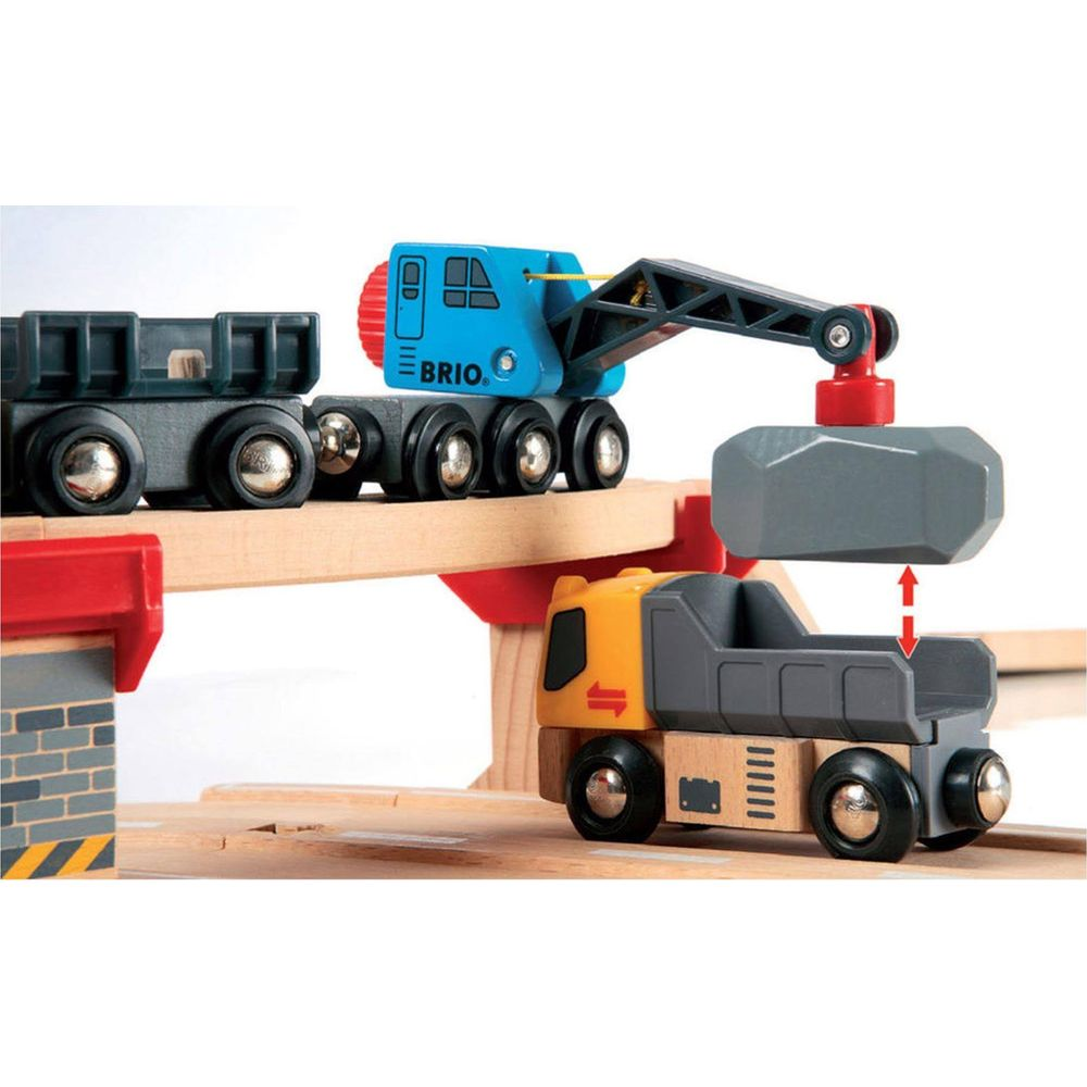 Ein Holz-Kranspielzeug hebt einen grauen Stein über einen gelben Lastwagen.