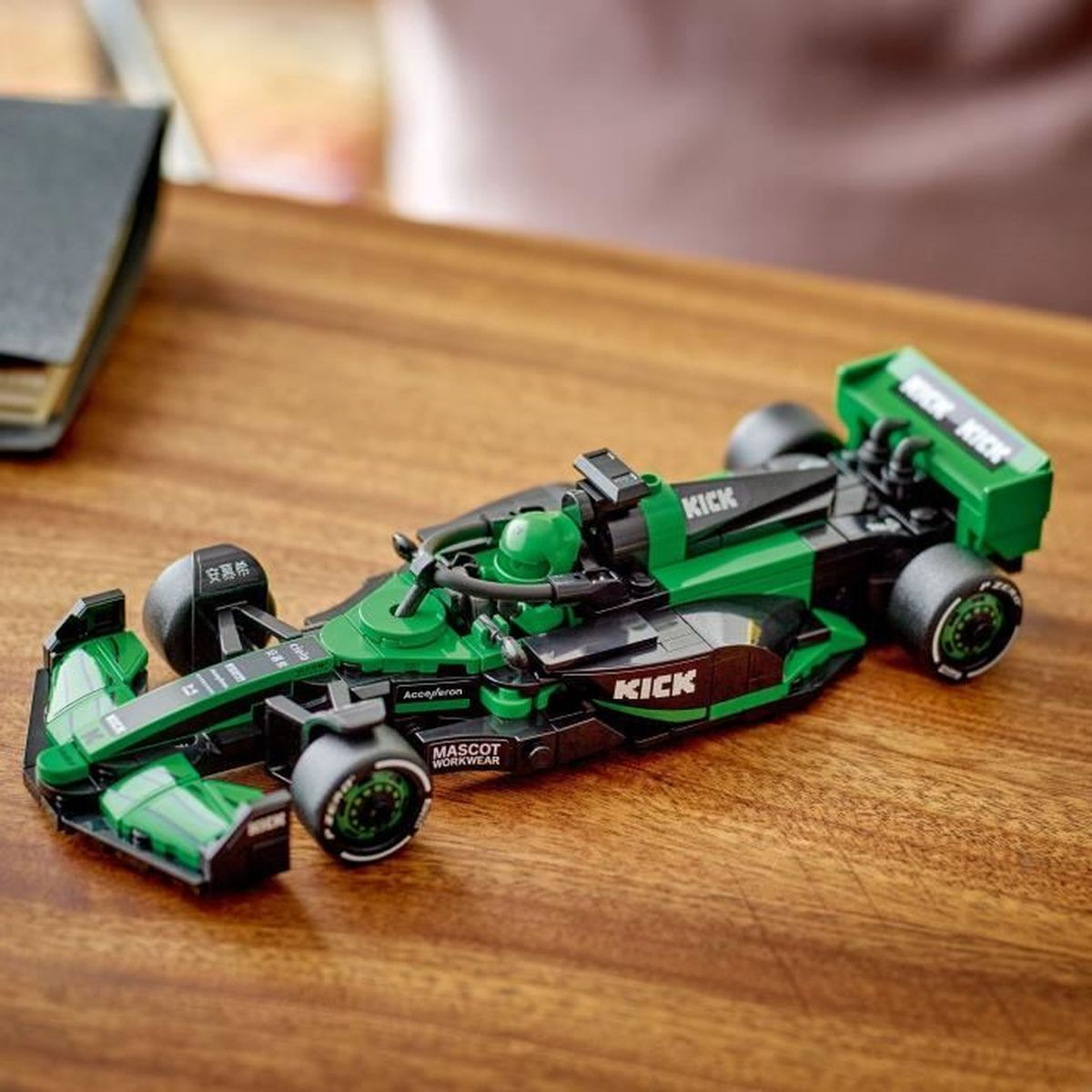 Ahşap masa üzerinde sponsor çıkartmalı yeşil ve siyah Lego yarış arabası.