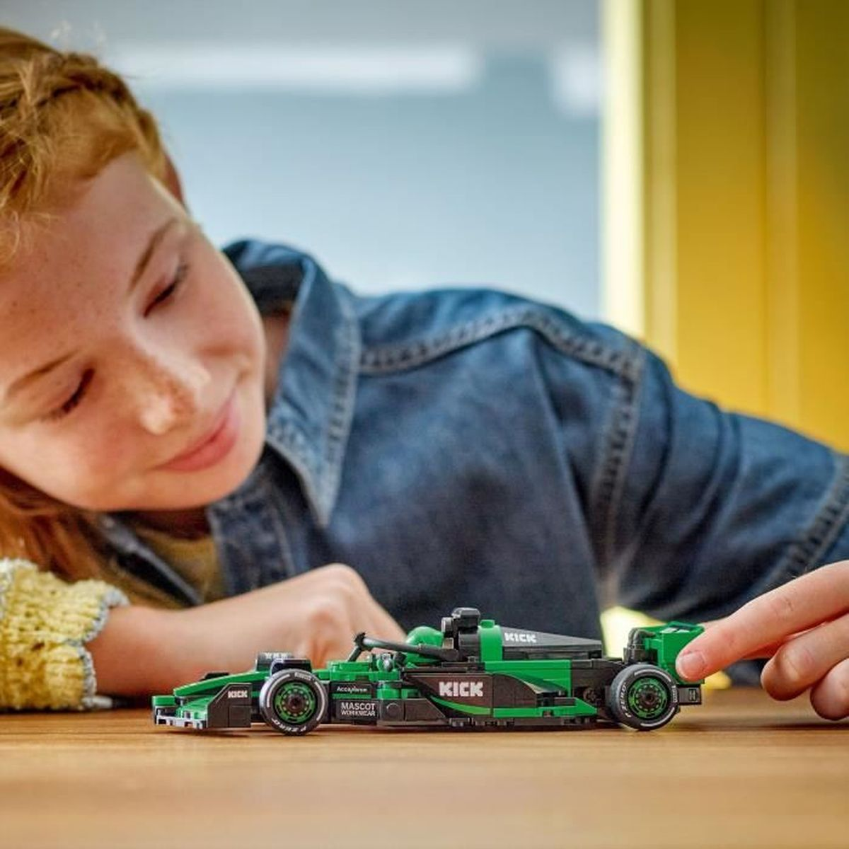 Kızıl saçlı bir kız, yeşil bir Lego yarış arabasıyla oynuyor.