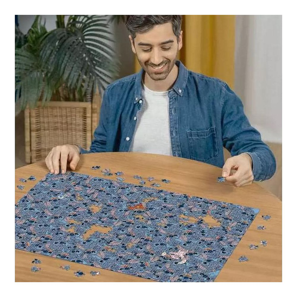Homme en chemise bleue faisant un puzzle sur une table en bois. Une plante est visible.