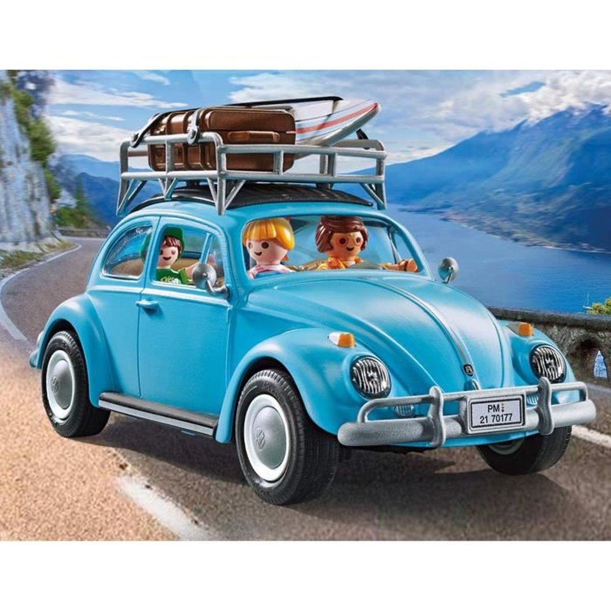 Ein blaues Käfer-Auto mit Gepäck auf dem Dach fährt auf einer Straße am See.