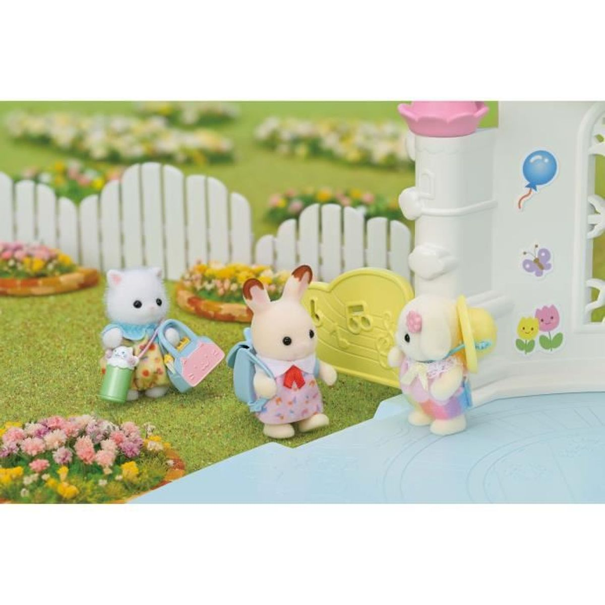 Drei Spielzeugtiere stehen im Freien vor einem weißen Zaun und Blumenbeeten.