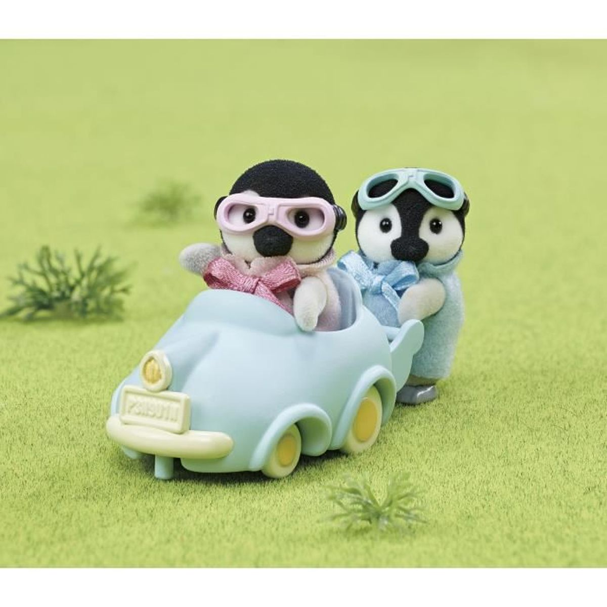 Dos pingüinos de juguete viajan en un coche azul claro sobre hierba verde.