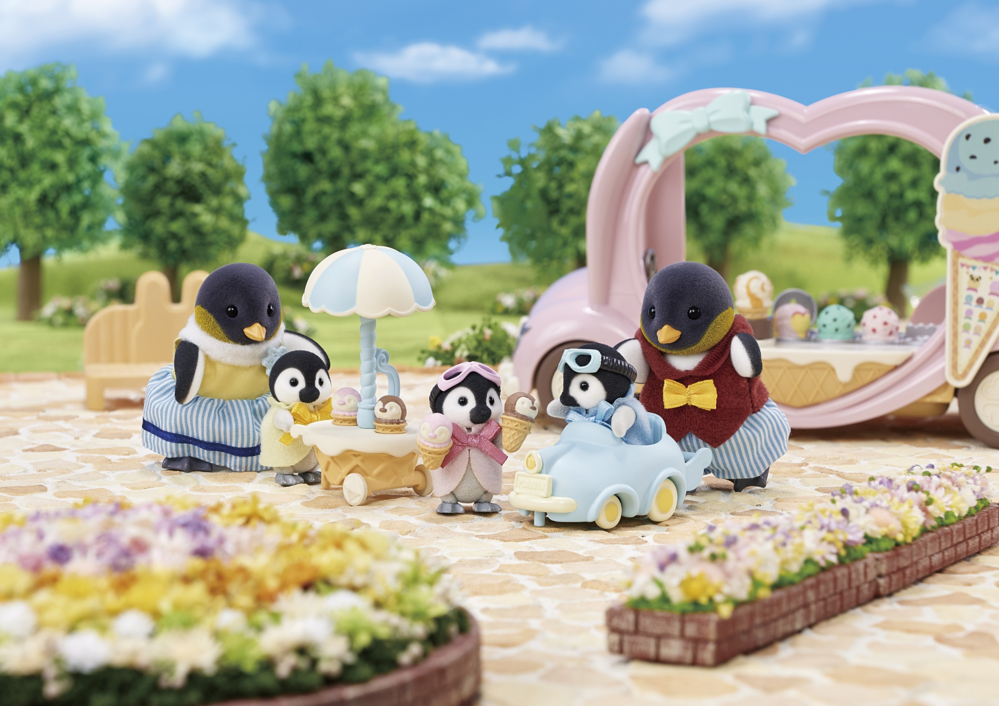 Pingüinos de juguete disfrutan de helado al aire libre, con un carrito de helados y flores.