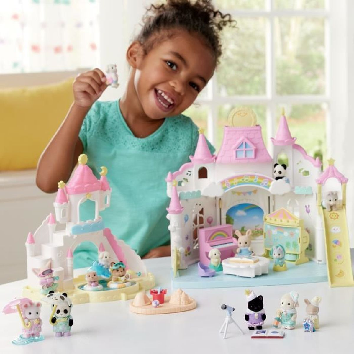 Una niña sonriente sostiene un animal de juguete. Un castillo de juguete rosa y blanco con animales de juguete está en la mesa.