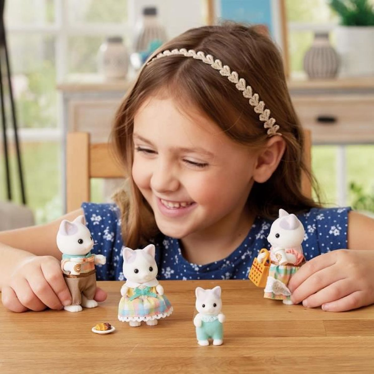 Niña jugando con figuritas de gatos en mesa de madera. Una figura tiene plato.